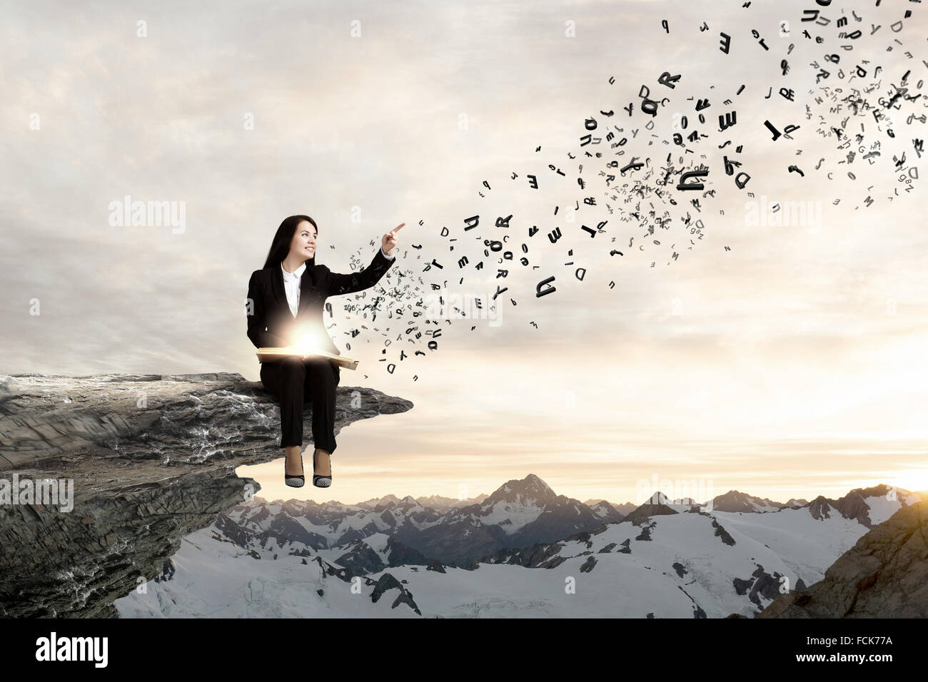 Young businesswoman sitting on rock edge with book in hands Stock Photo