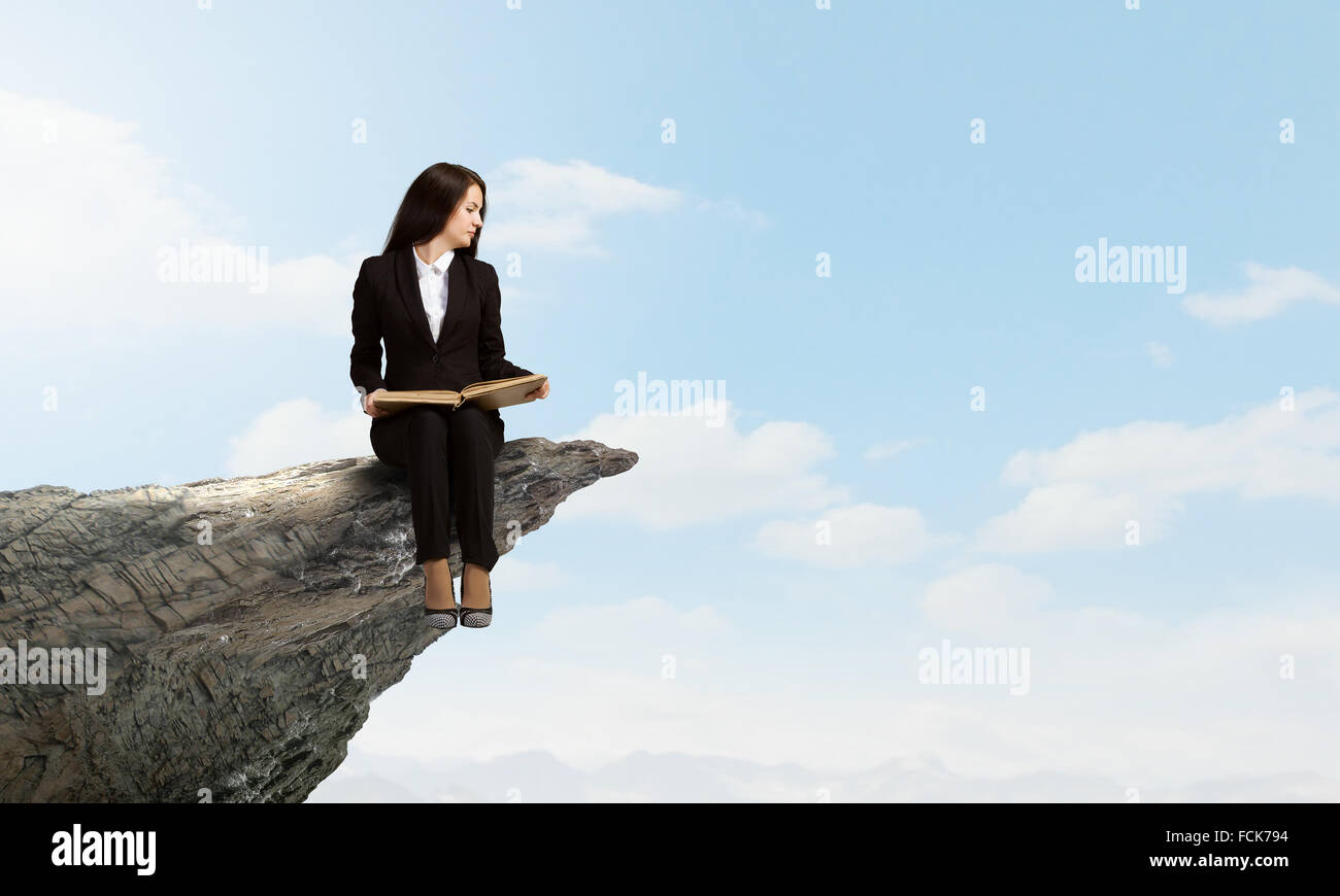 Young businesswoman sitting on rock edge with book in hands Stock Photo