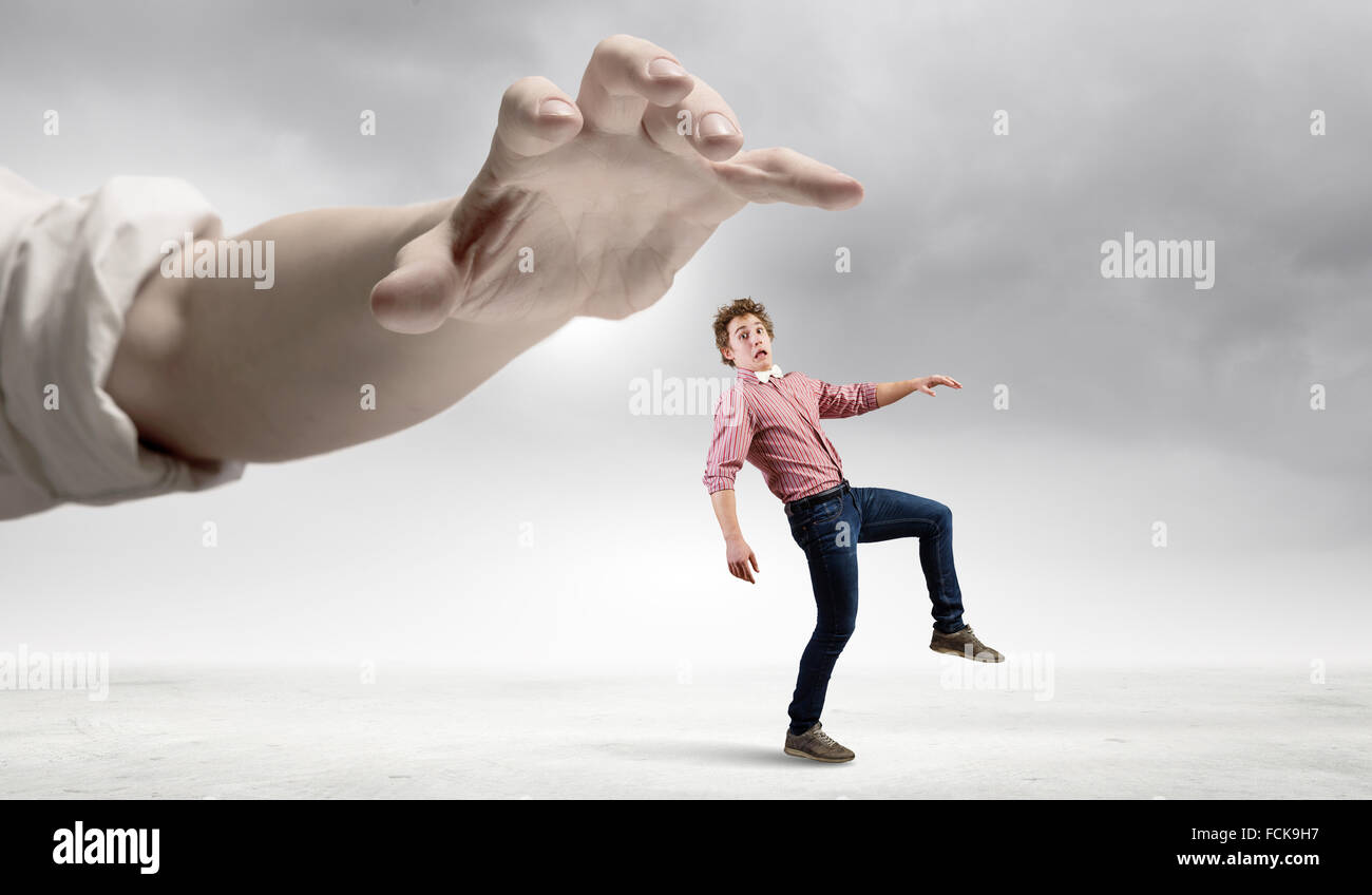 Young man in casual running away from big hand Stock Photo