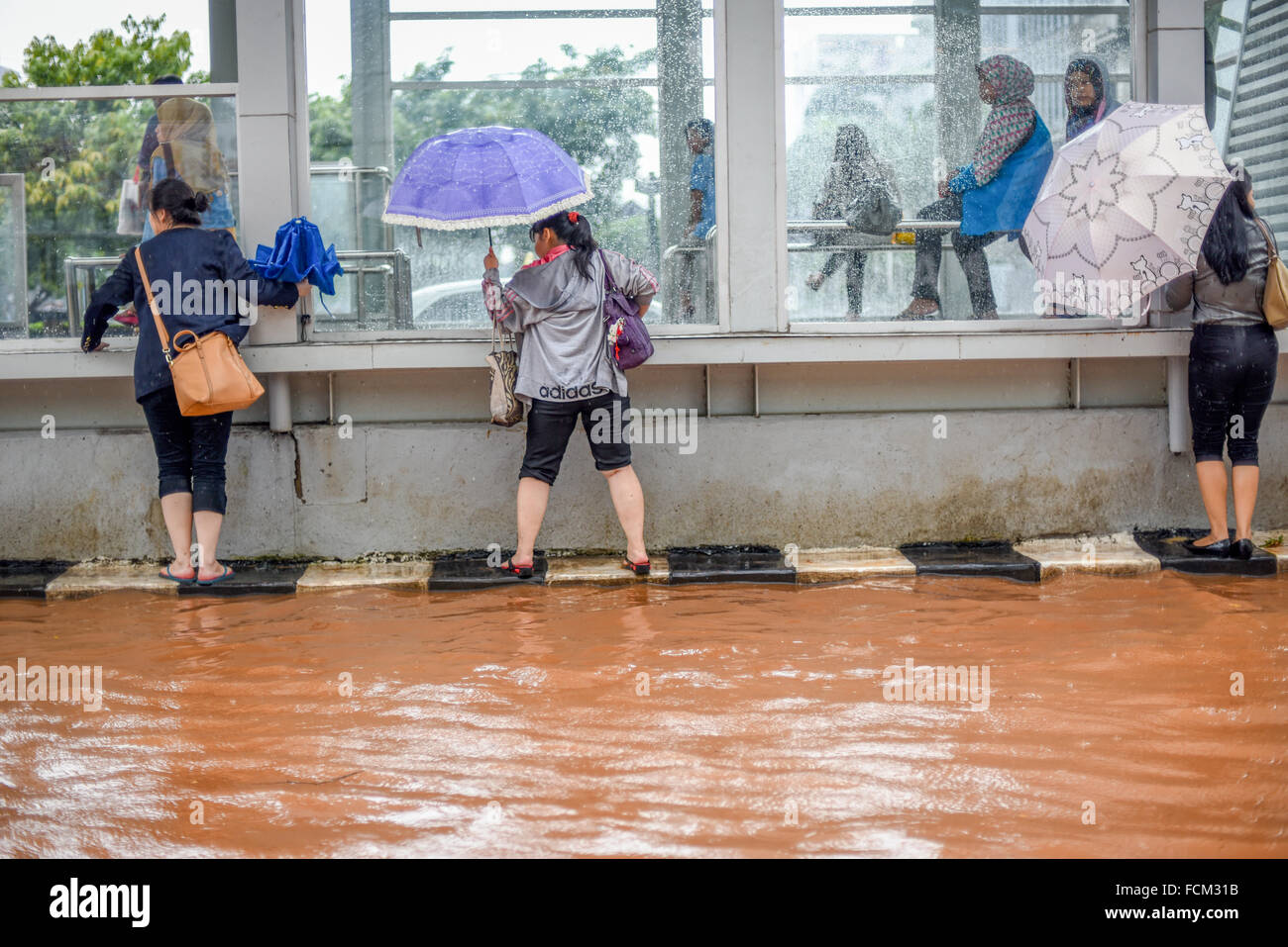 Pedestrians trying to avoid floodwater as they are walking, by hanging on the side of a Trans Jakarta bus station on Thamrin Street, Jakarta. Stock Photo
