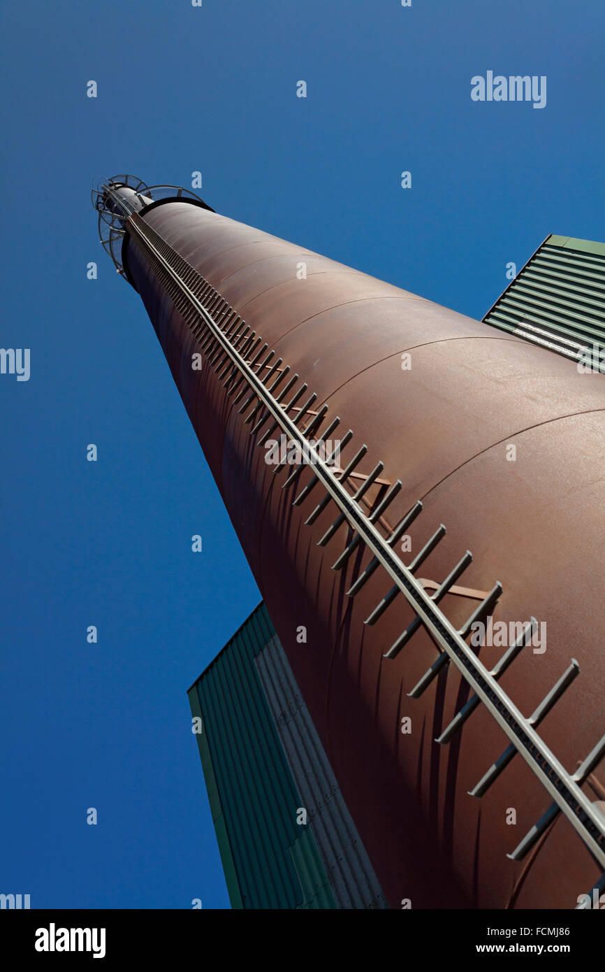 A tall steel smokestack at a processing plant for fish oil. against blue sky and green building Stock Photo