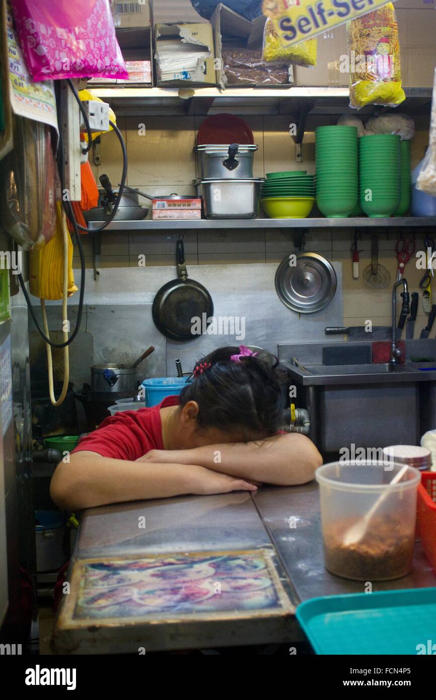 Asian woman with head in her arms falling asleep in her food stand