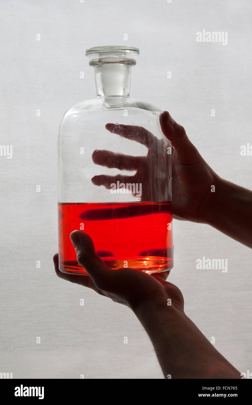 hands hold an antique glass flask containing red liquid Stock Photo Alamy