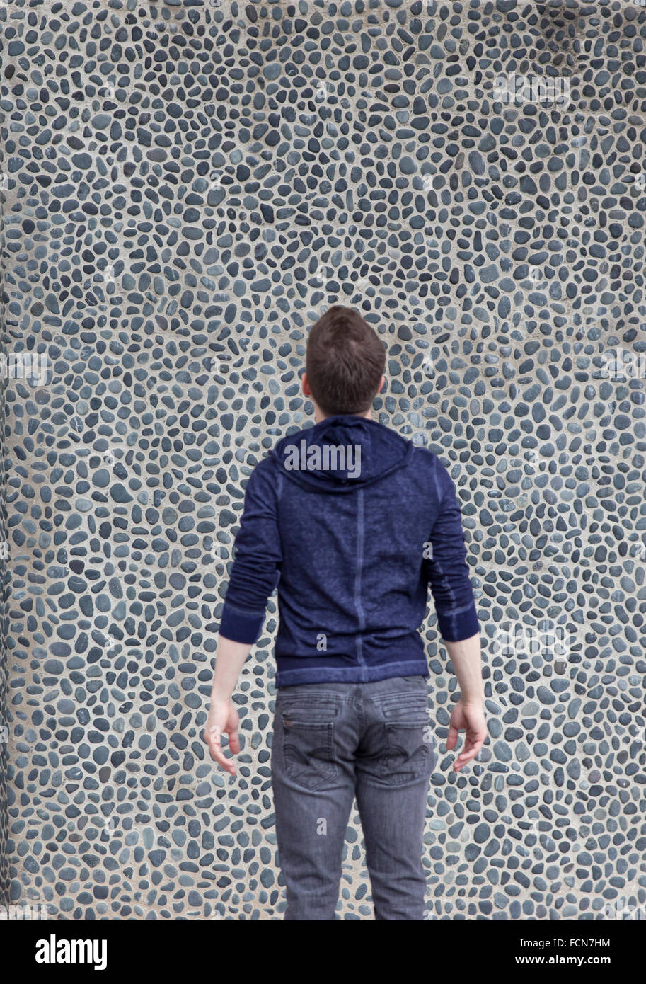 man looks at wall full of small stones in busy pattern Stock Photo