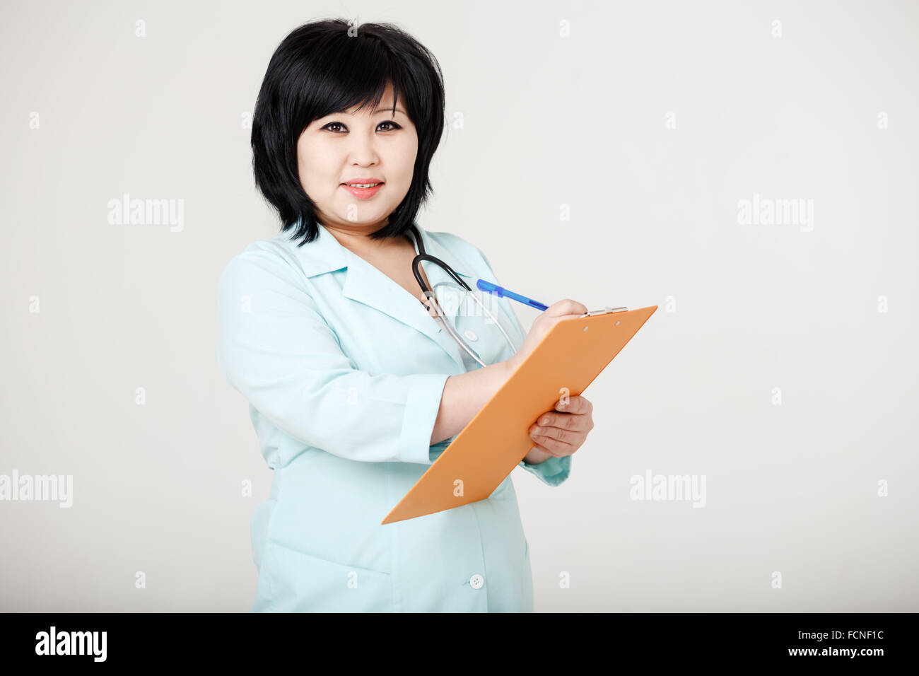 Asian brunette nurse with stethoscope around neck and folder in her hands ready to record patient information, provides diagnosis. Registry, medical data entry, record. On reception at doctor. Stock Photo