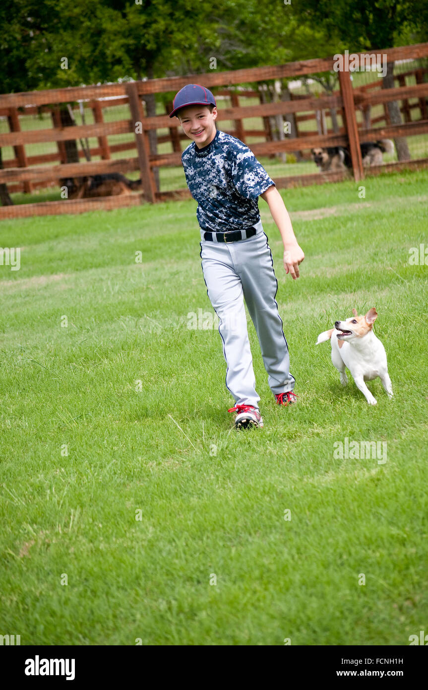 Youth baseball player playing with his dog in the yard outdoors. Stock Photo