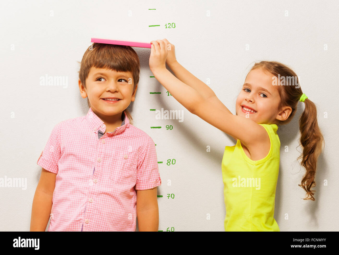 Boy and girl measure height by wall scale at home Stock Photo