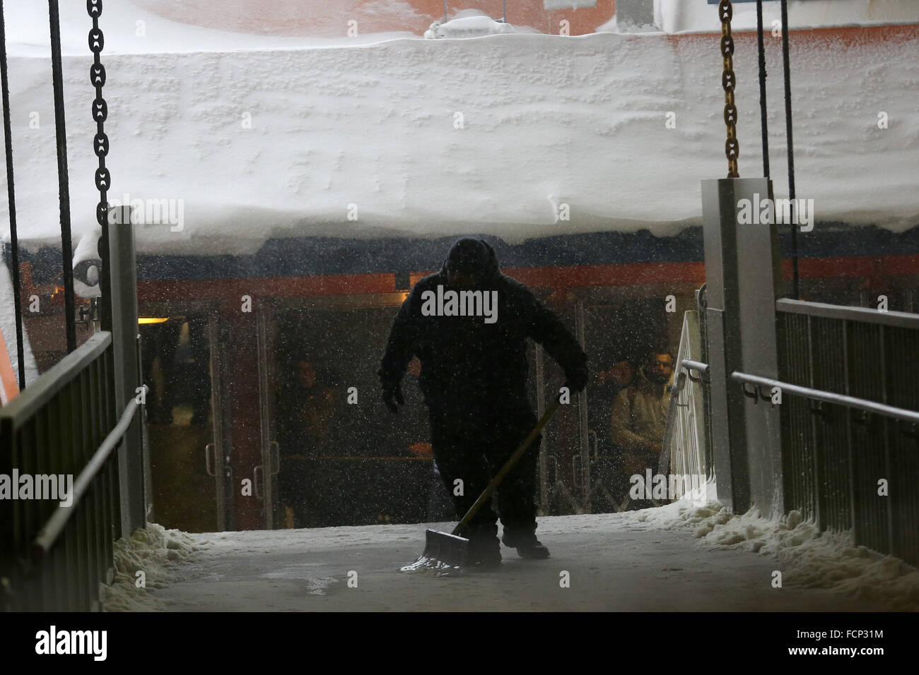 New York, New York, USA. 23rd Jan, 2016. A DOT employee removes snow off of the ramp before passengers depart the Staten Island Ferry in St. George terminal during Winter Storm Jonas. A travel ban had been in place for hours, but the ferry still operated. Snowfall projections for Staten Island were approximately 12-18in, with winds gusting up to 50 miles an hour. Late afternoon, buses ceased to run and a travel ban was enforced by the NYPD. This lack of transportation stranded many residents of Staten Island who had taken the ferry home. People were forced to try and walk to their destination Stock Photo