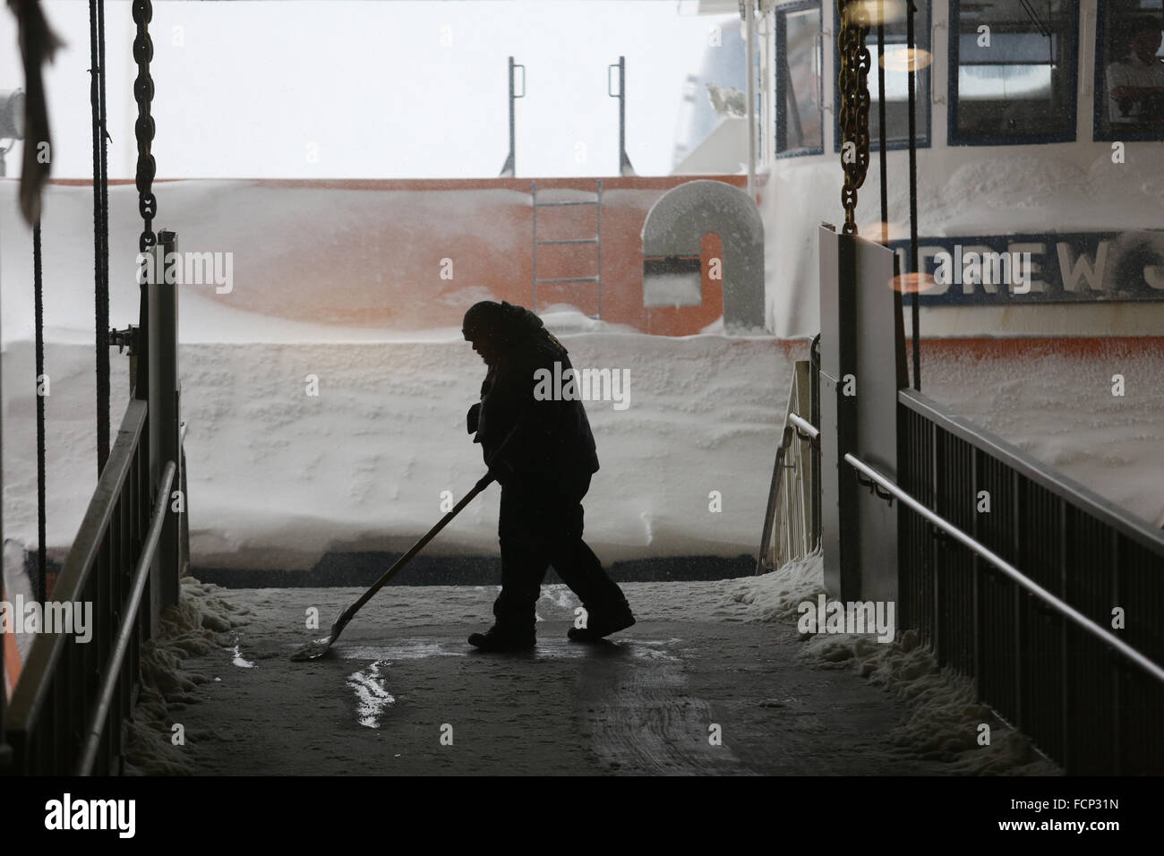 New York, New York, USA. 23rd Jan, 2016. A DOT employee removes snow off of the ramp before passengers depart the Staten Island Ferry in St. George terminal during Winter Storm Jonas. A travel ban had been in place for hours, but the ferry still operated. Snowfall projections for Staten Island were approximately 12-18in, with winds gusting up to 50 miles an hour. Late afternoon, buses ceased to run and a travel ban was enforced by the NYPD. This lack of transportation stranded many residents of Staten Island who had taken the ferry home. People were forced to try and walk to their destination Stock Photo