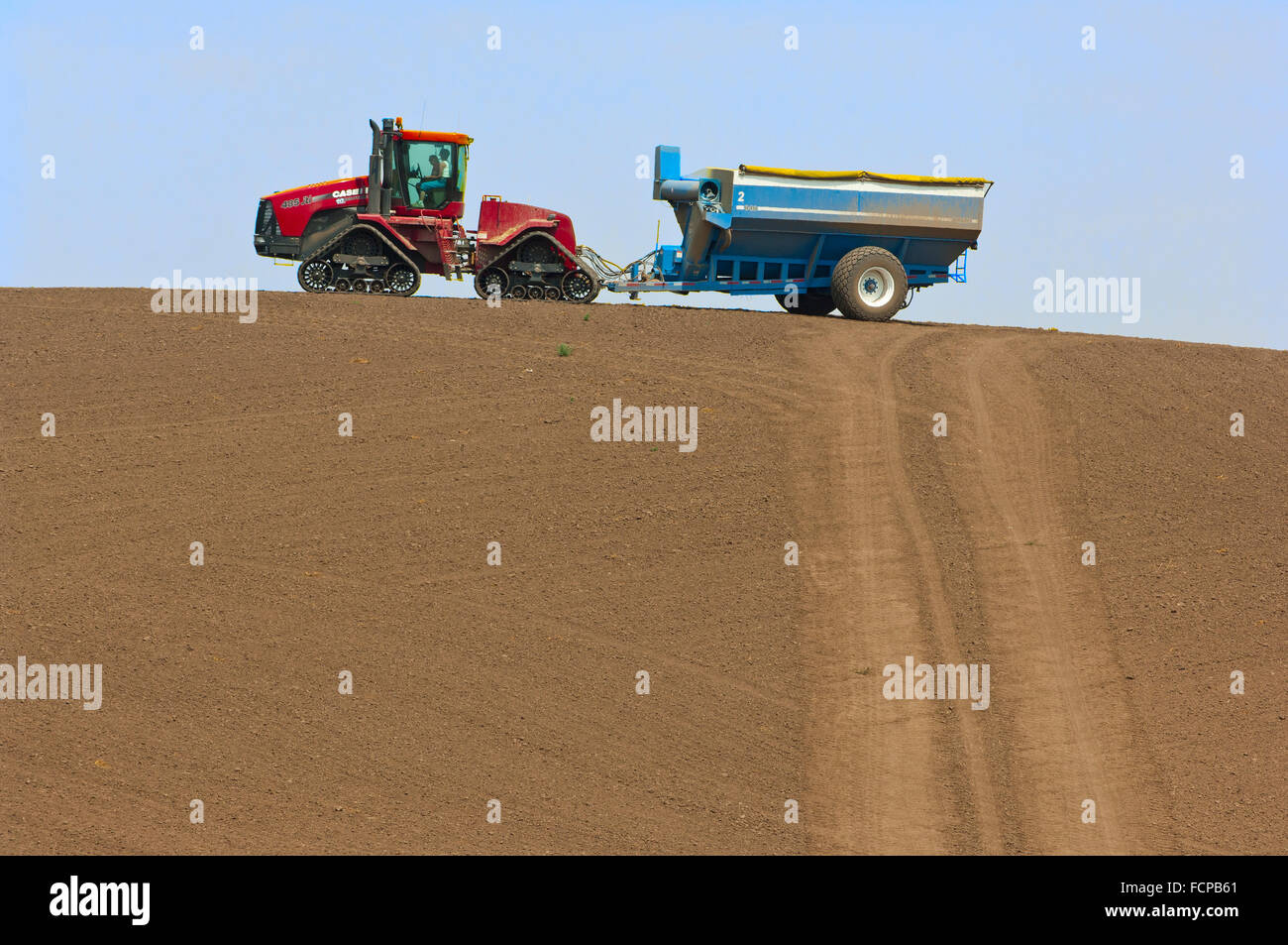 A tractor pulling a grain cart traverses a ridge top during harvest in the Palouse region of Washington Stock Photo