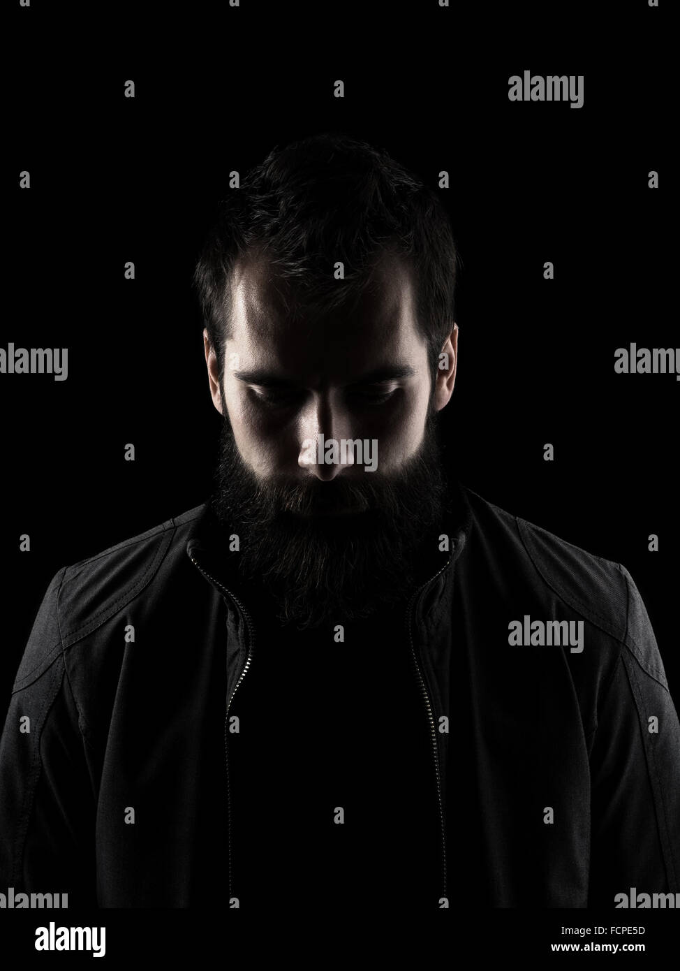 Sad bearded man looking down. High contrast low key dark shadow portrait isolated over black background. Stock Photo