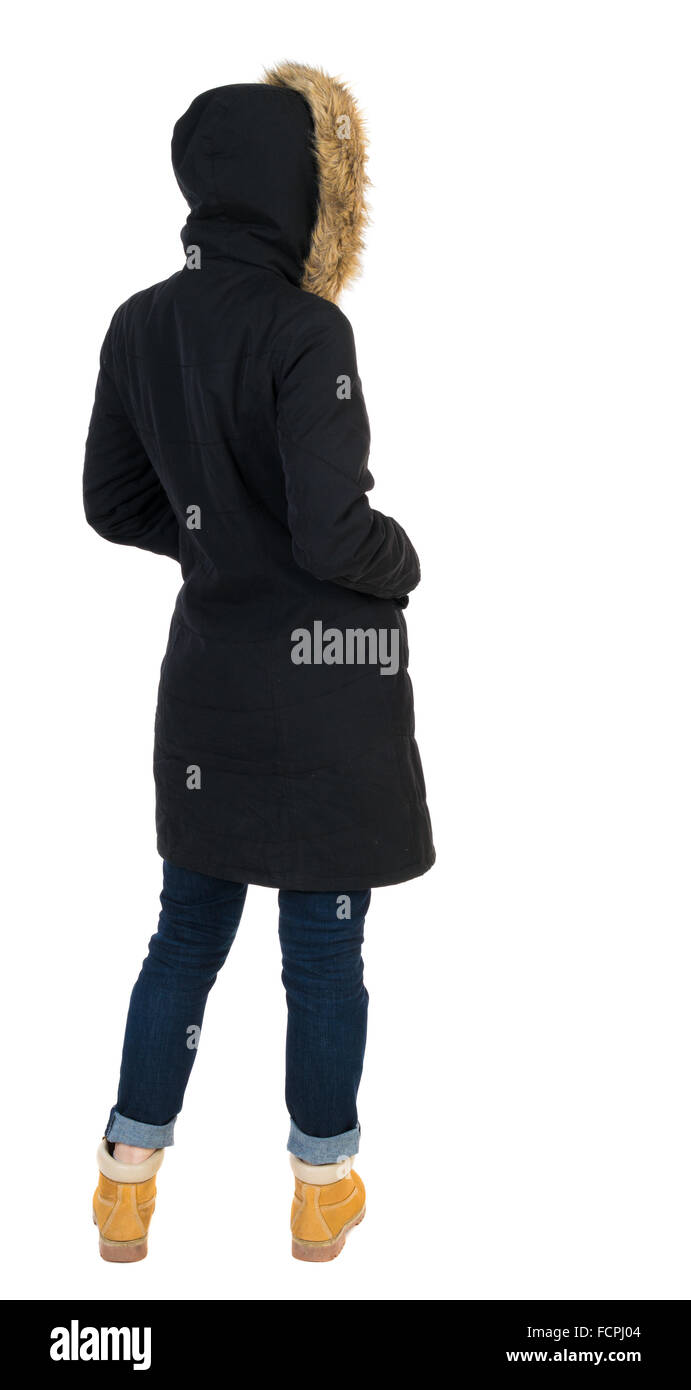 Back view woman in winter jacket looking up. Standing young girl in parka. Rear view people collection. backside view of person. Isolated over white background. Girl in a black winter jacket with a hood looking to the right with his hands in his pockets. Stock Photo