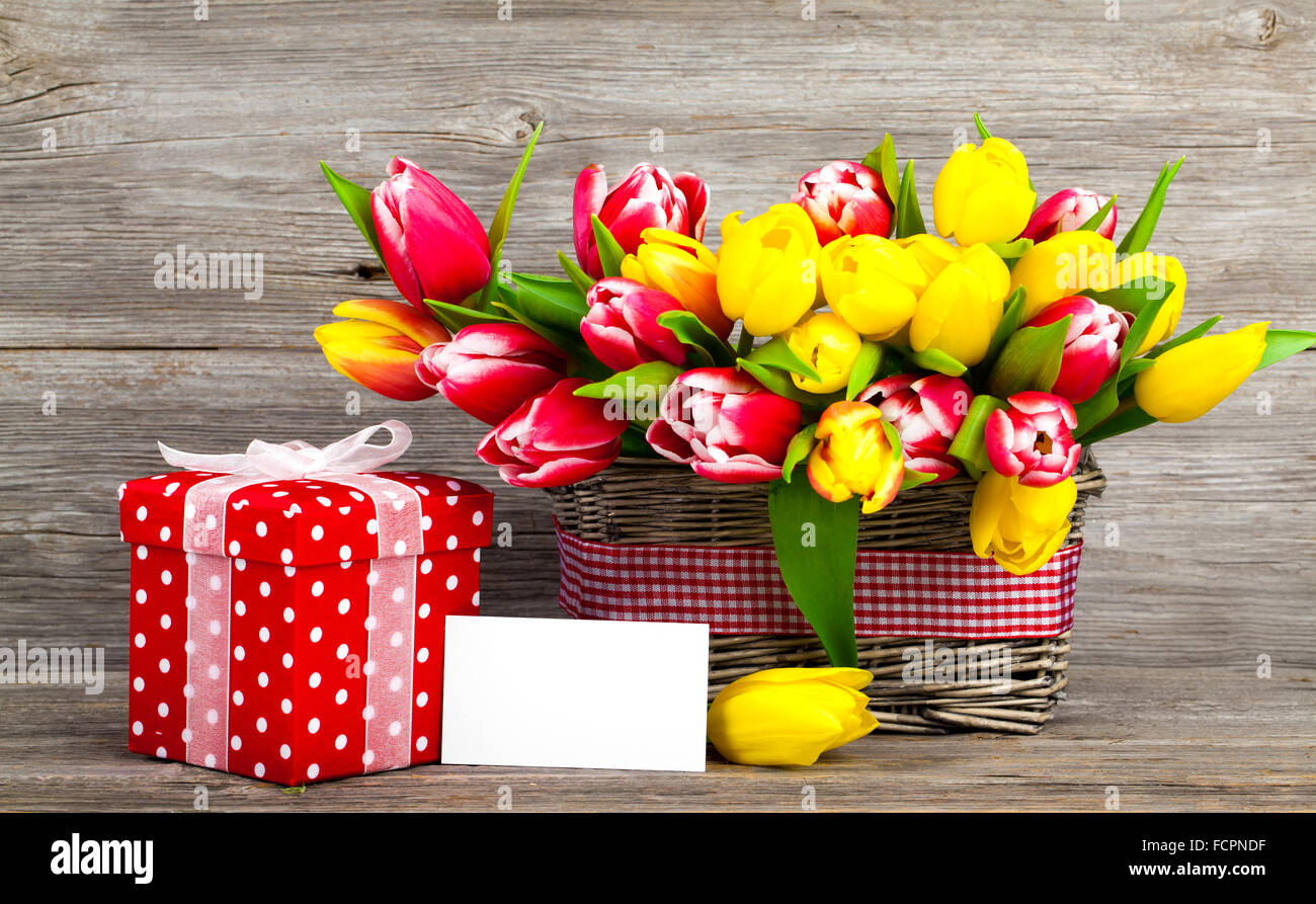 spring tulips in wooden basket, red polka-dot gift box. happy mothers day, romantic still life, fresh flowers. on wooden. Stock Photo