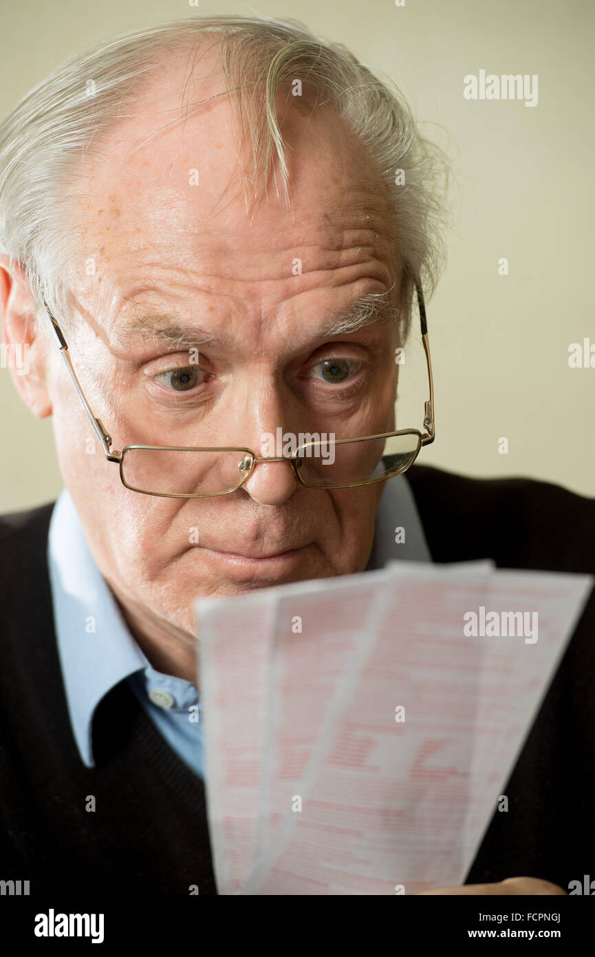 An elderly man looks over his glasses in a confused way at lottery tickets Stock Photo