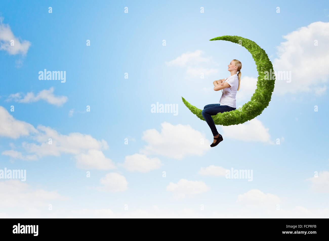 Young girl sitting on green moon high in sky Stock Photo