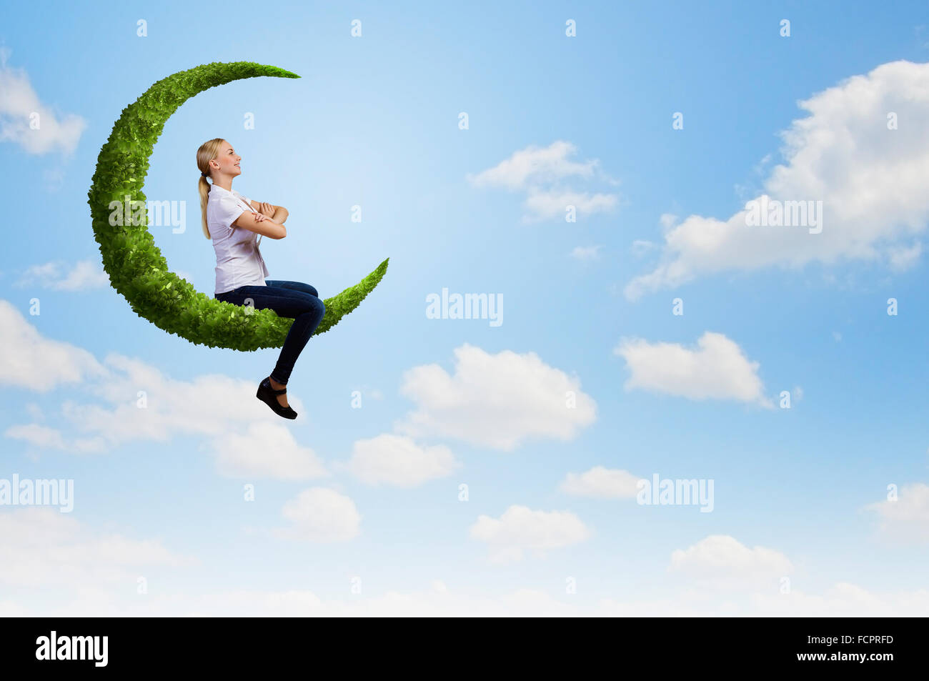 Young girl sitting on green moon high in sky Stock Photo