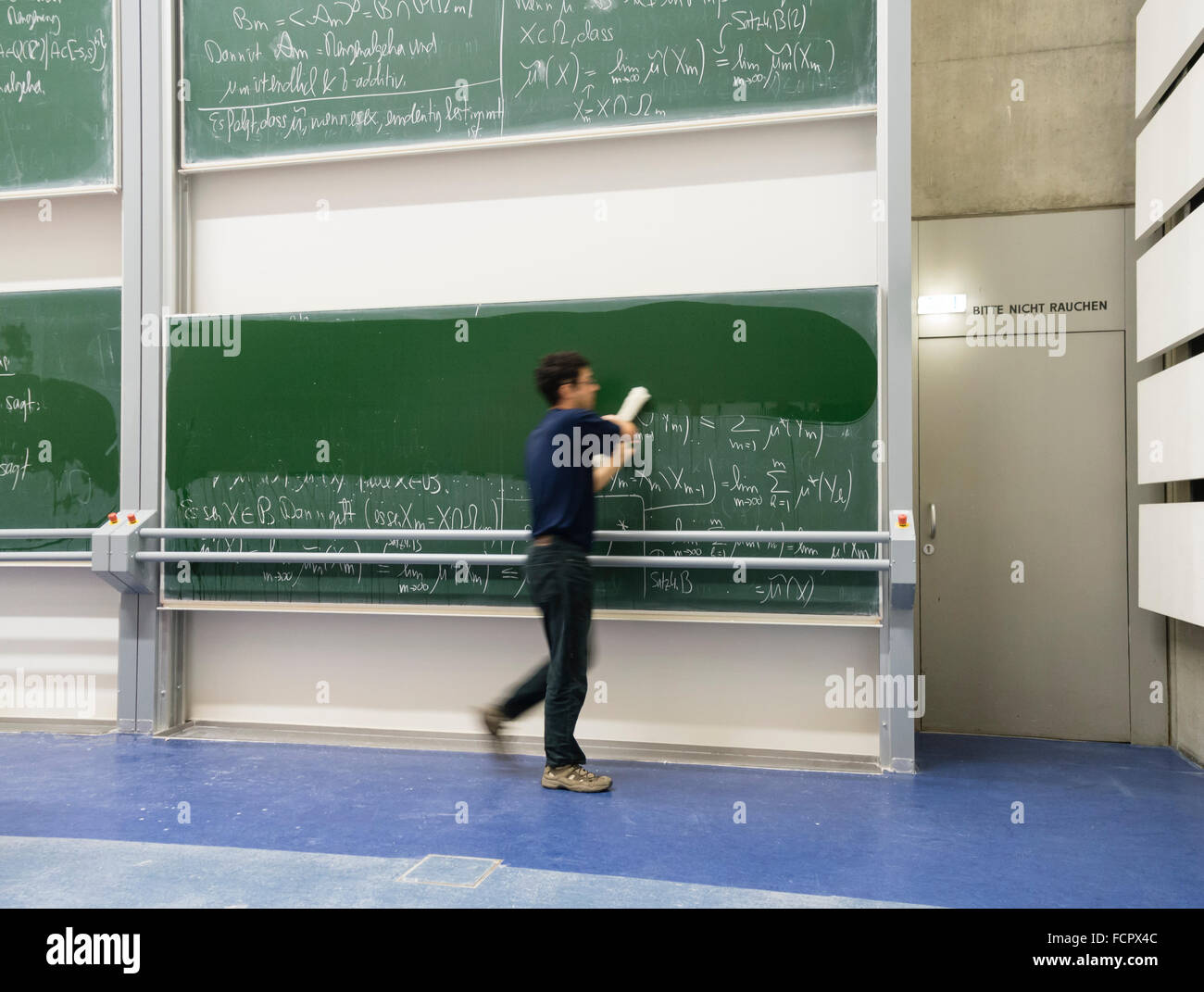 Professor wiping away scientific formulas from large double blackboard at university. Stock Photo