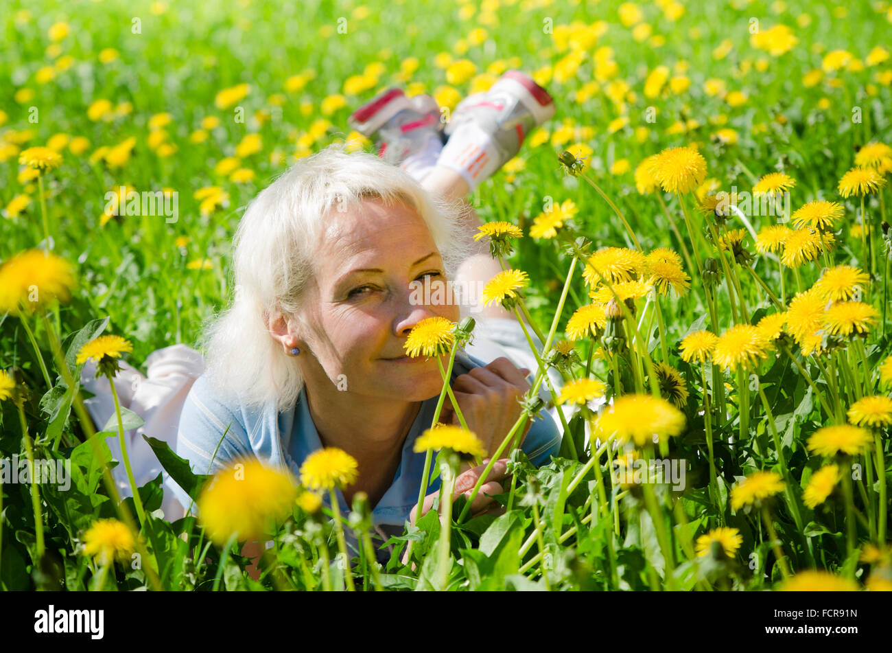 A woman lies in a clearing among the dandelions and sniffs a flower Stock Photo