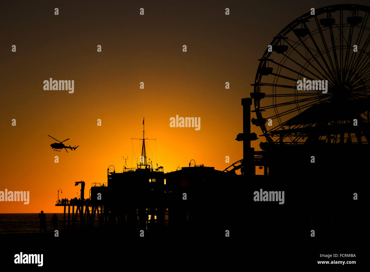 A helicopter passes Santa Monica pier at sun set Stock Photo