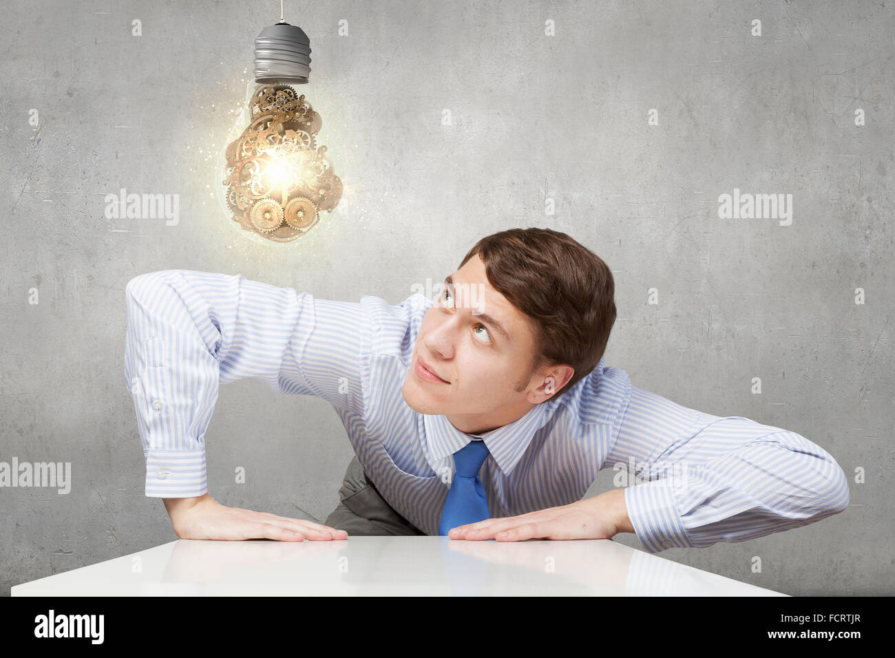 Young man looking from under table on light bulb Stock Photo - Alamy