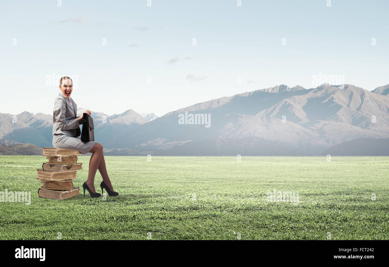 Young woman sitting on pile of books with book in hands Stock Photo - Alamy