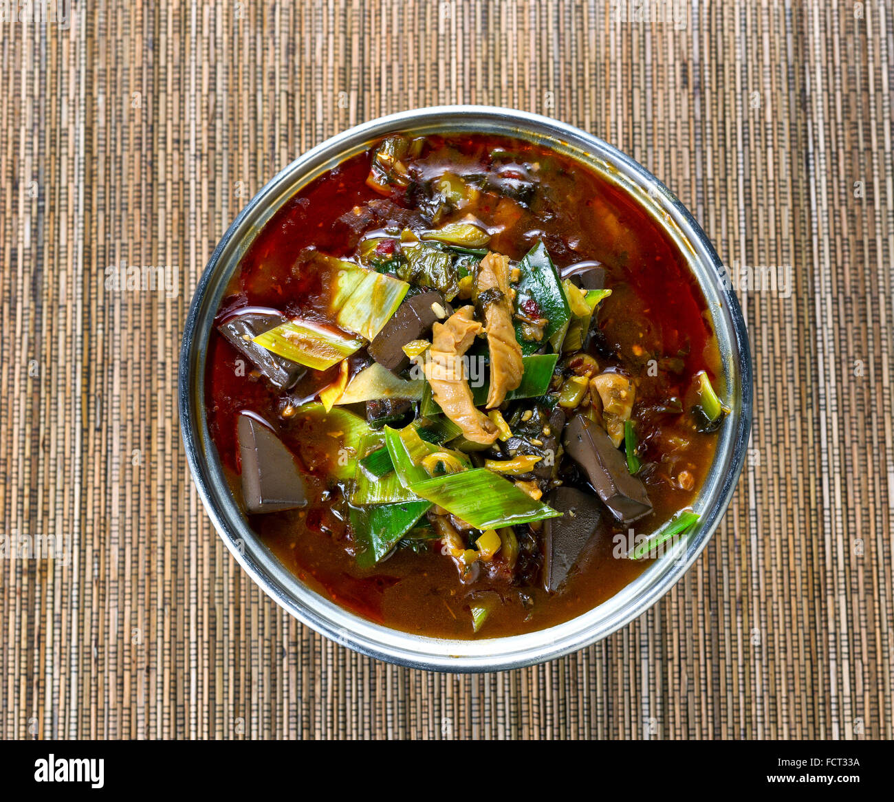High angled view of a cooking pot filled with vegetables, spicy pepper sauce and tofu for soup dinner on bamboo mat. Stock Photo