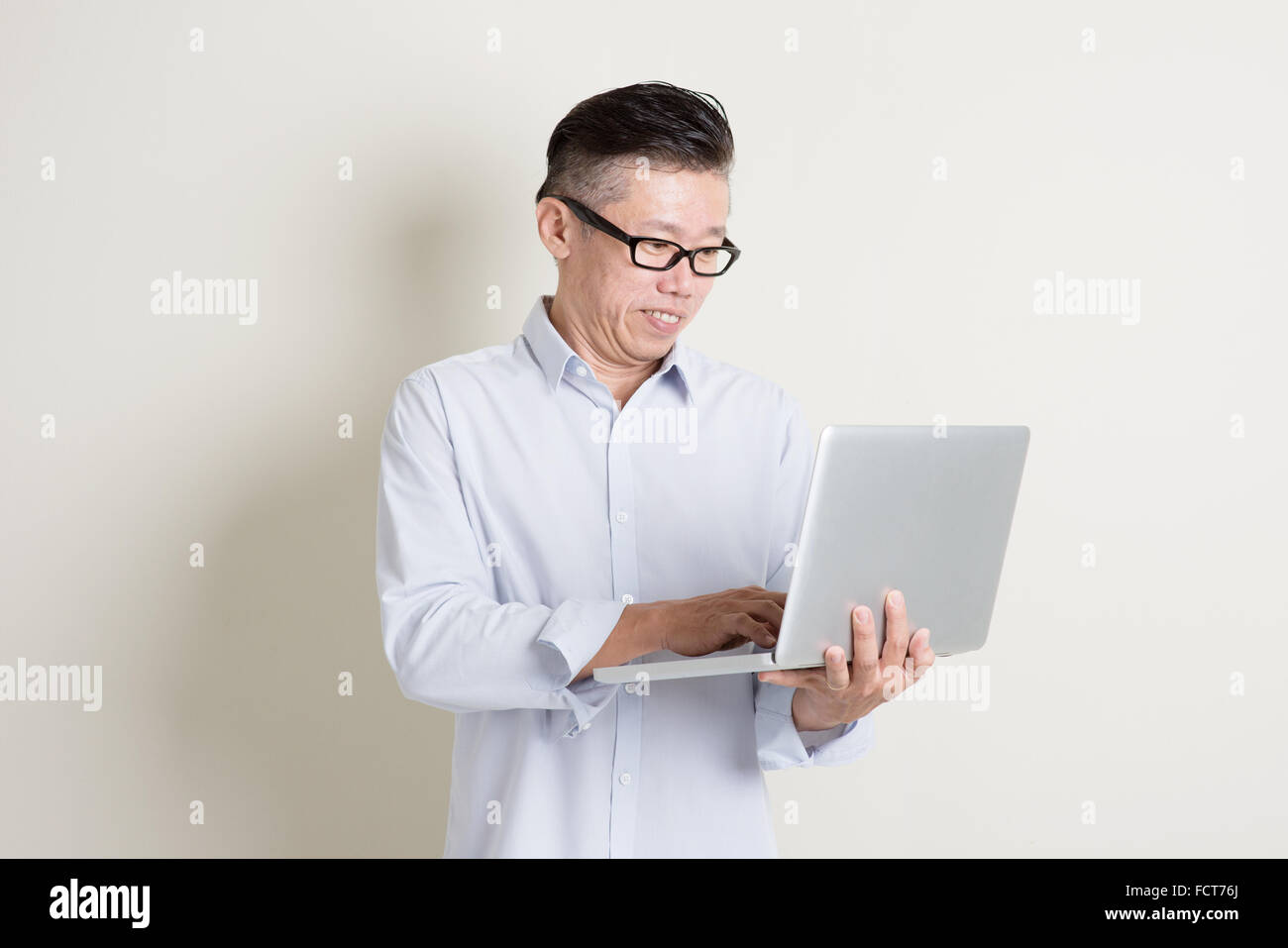 Portrait of single mature 50s Asian man in casual business using laptop ...