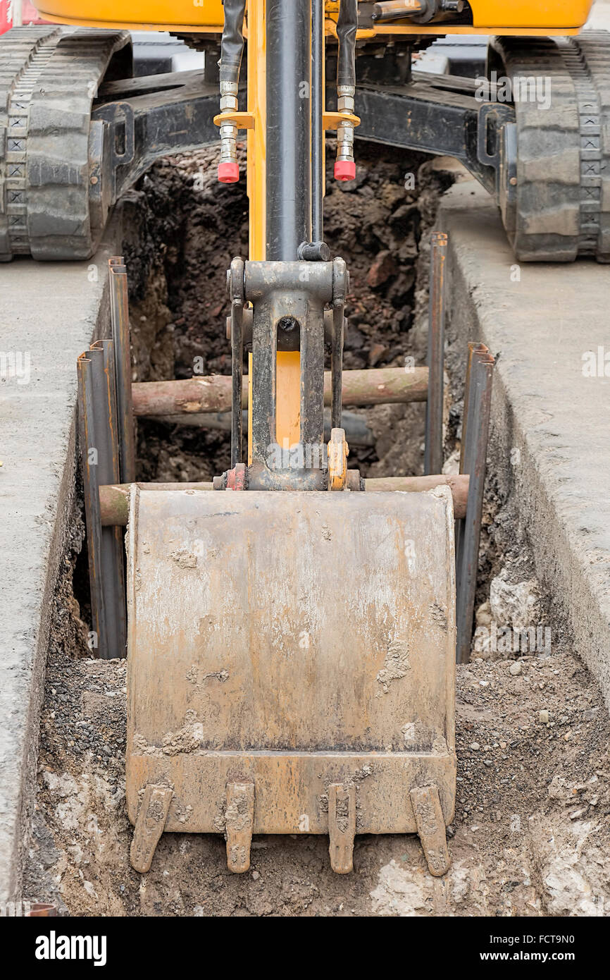 Small digger in city digging trench, utility repair Stock Photo