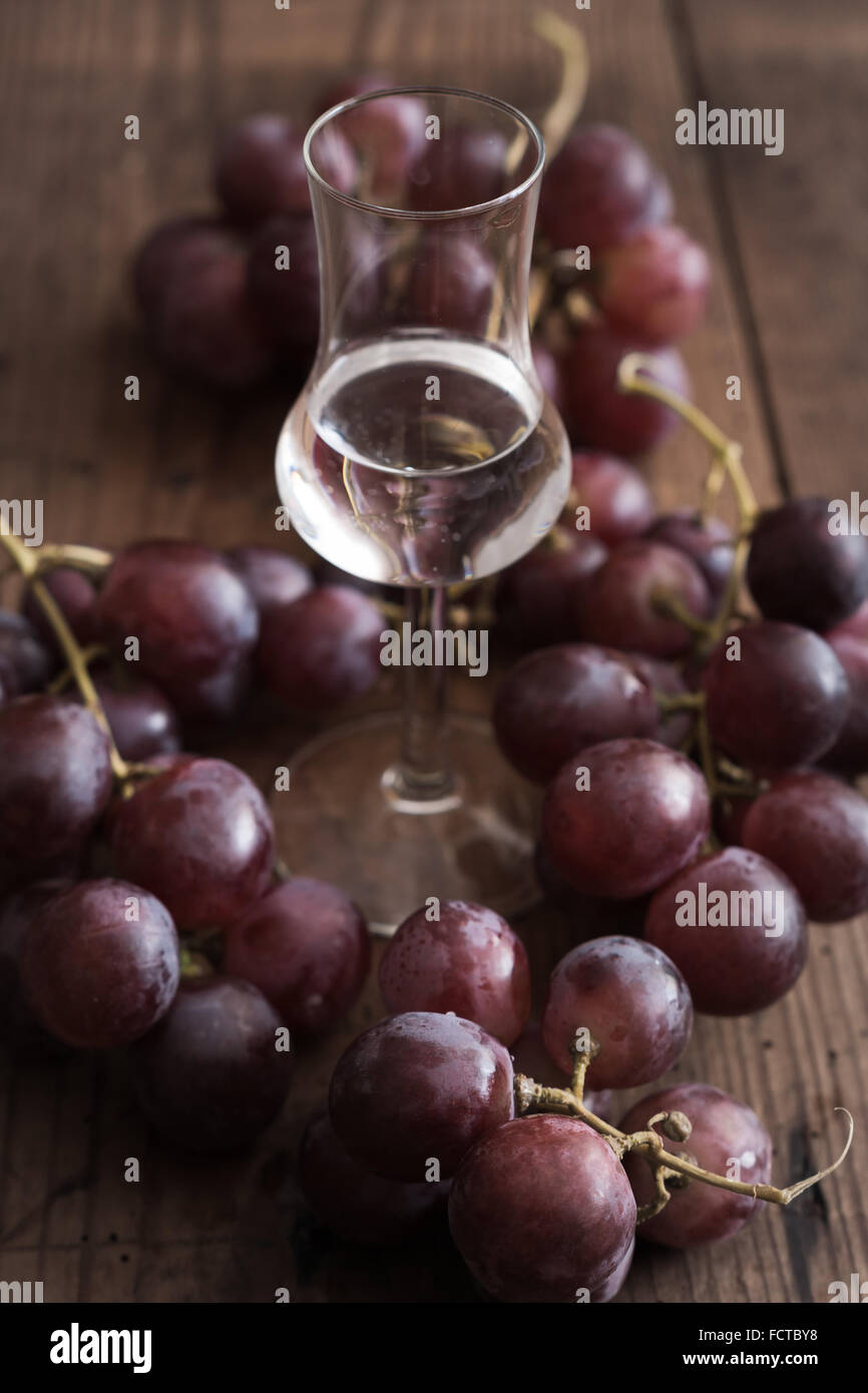 Glass of Grappa with Grape on a wooden Table Stock Photo