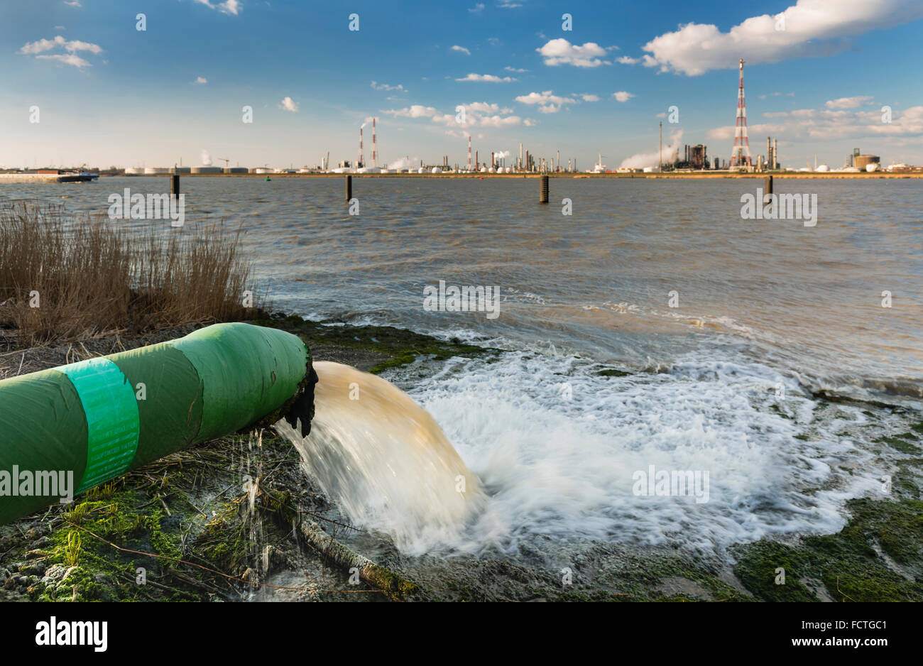 A wastewater pipe and a large oil refinery in the harbor of Antwerp, Belgium with blue sky and warm evening light. Stock Photo