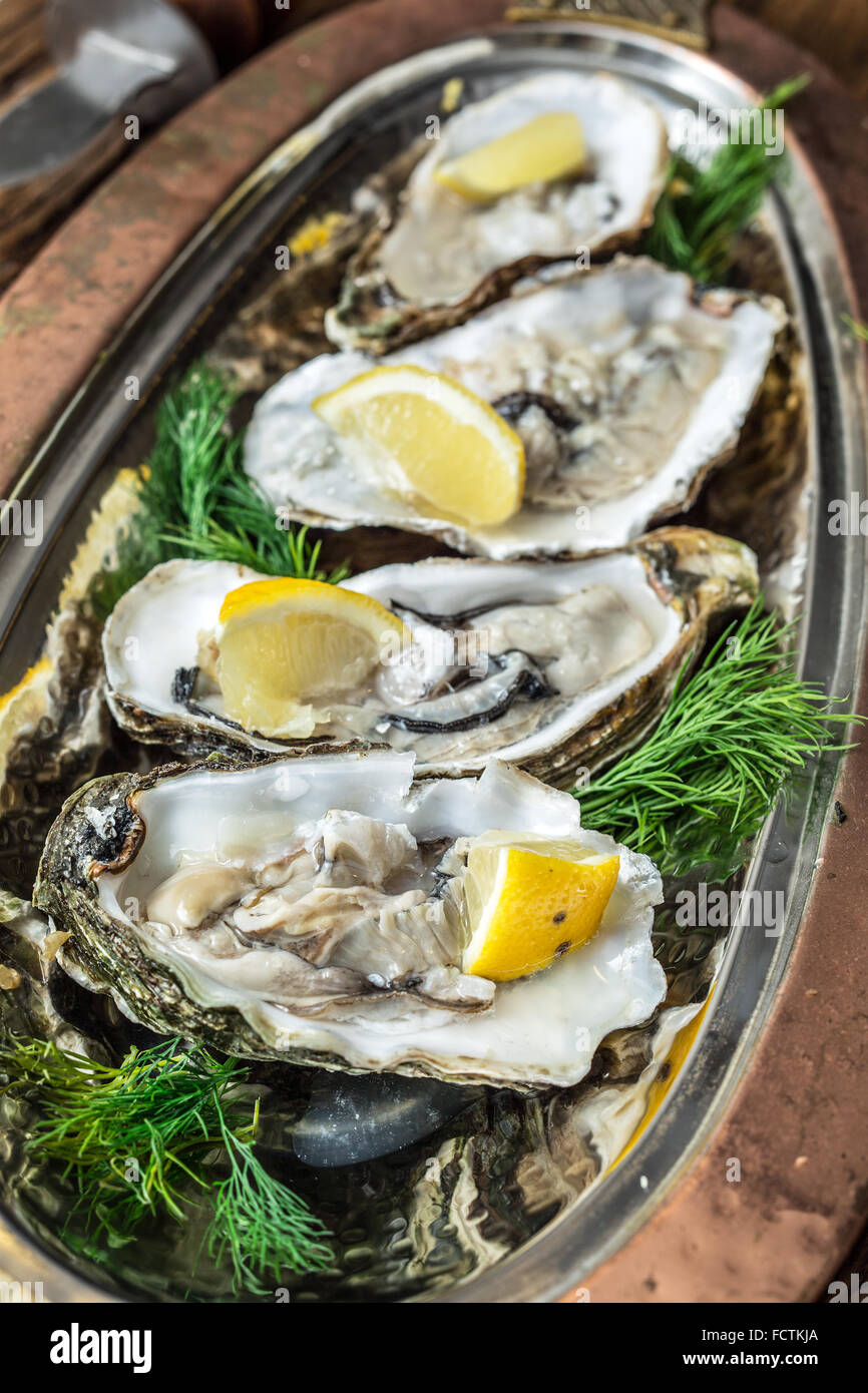 Opened oysters with piece of lemon on the cooper tray. Stock Photo