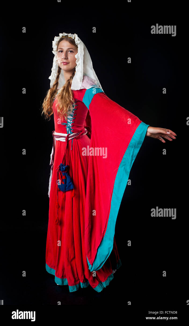 Studio portrait of medieval girl in a red dress and head scarf on black background Stock Photo