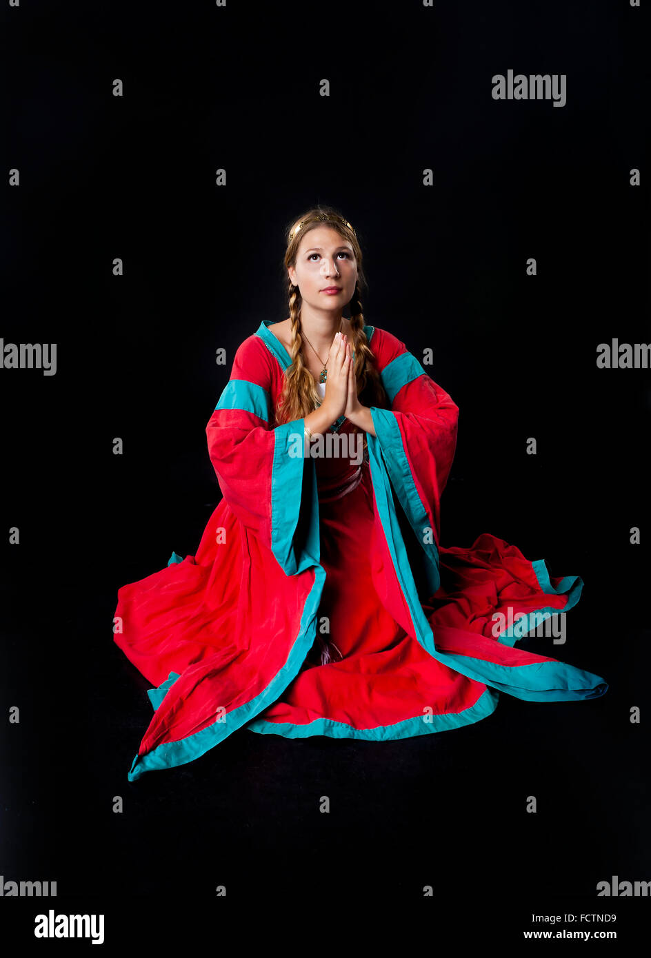 Studio shot of a beautiful young girl in medieval clothing kneeling to pray (on black background) Stock Photo