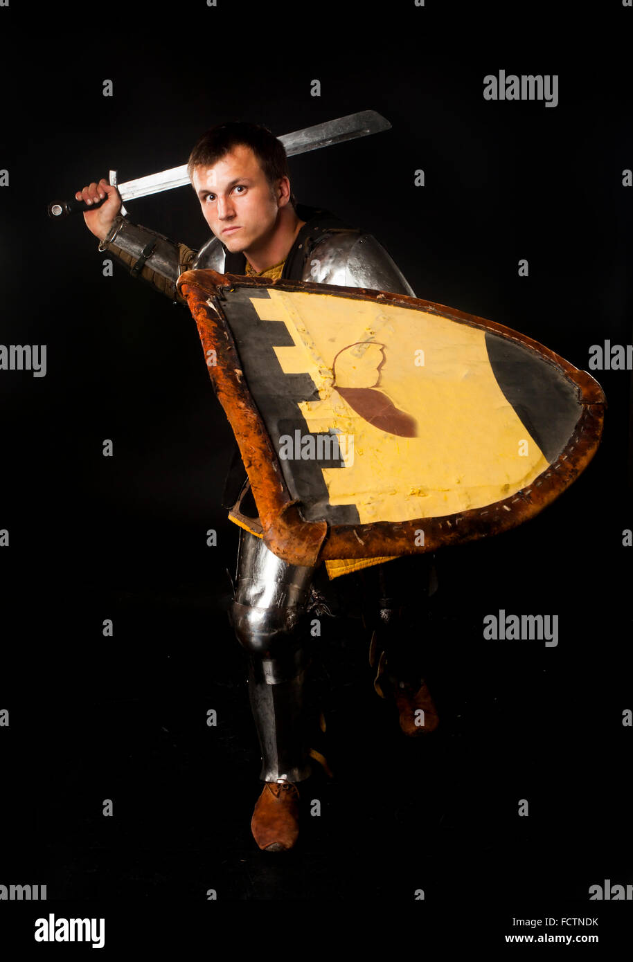 Studio shot of young man dressed as medieval knight swinging his sword