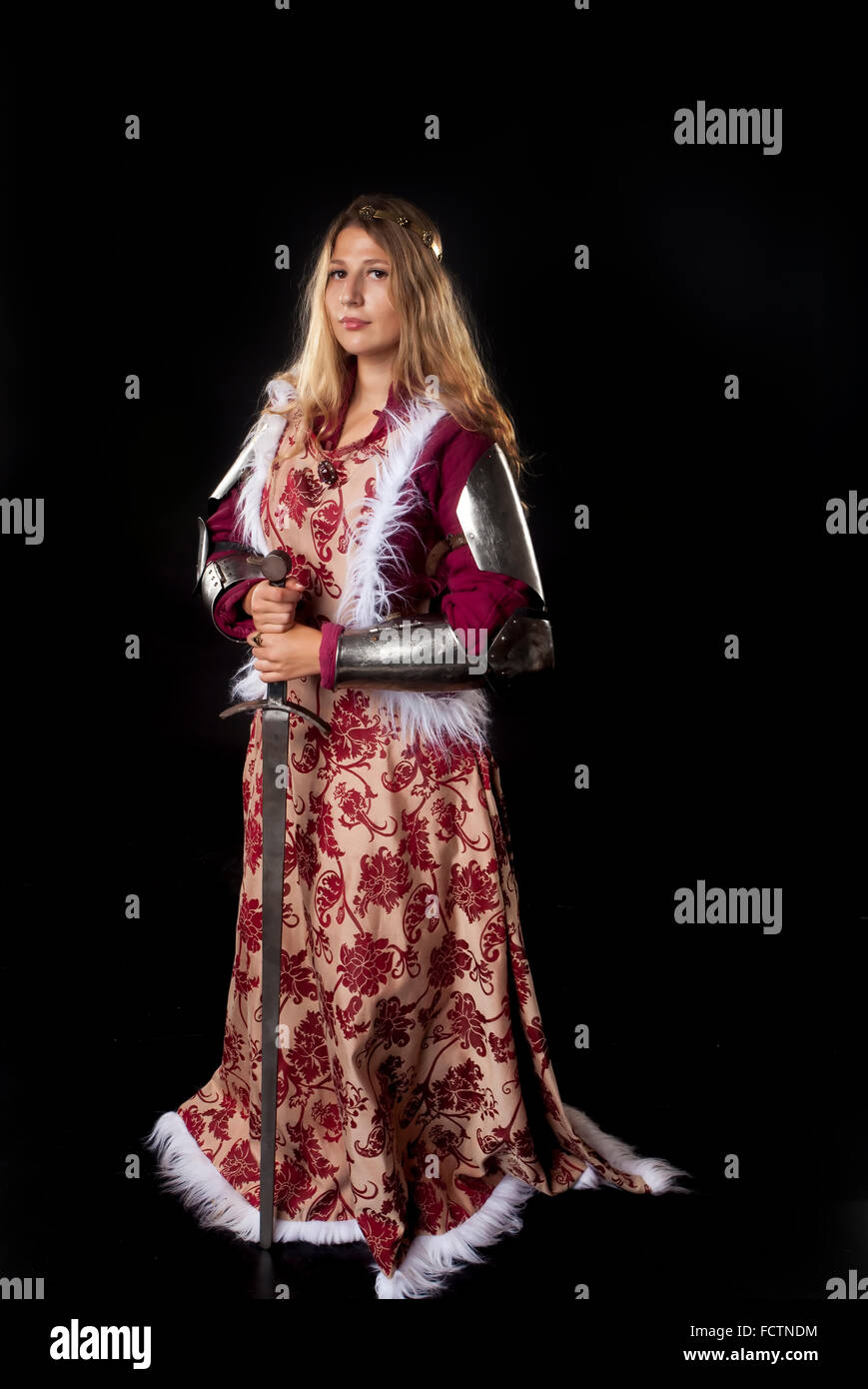 Studio portrait of medieval girl with golden hair and royal posture leaning on a sword Stock Photo