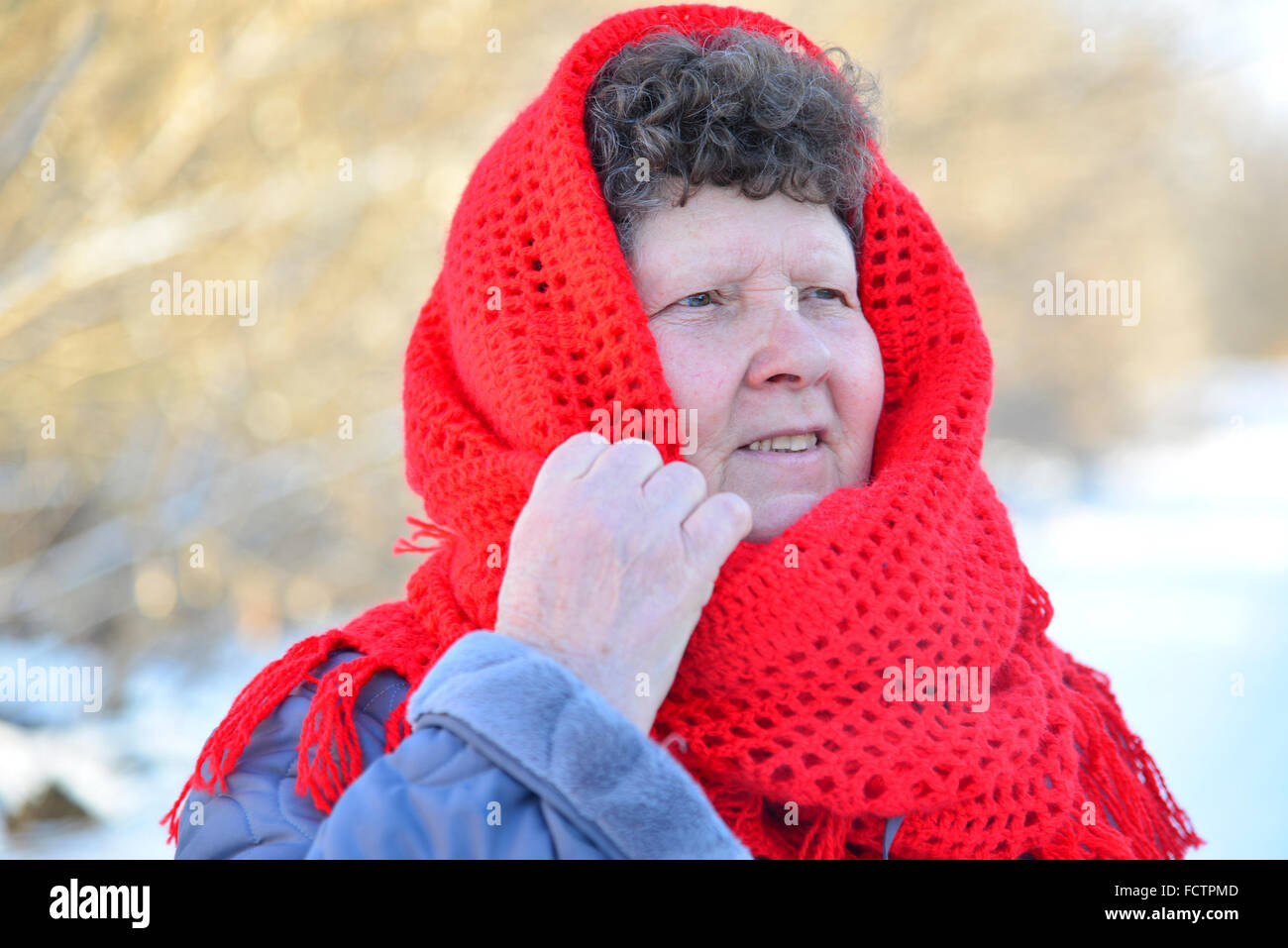Elderly woman in red knitted scarf on her head outdoors Stock Photo