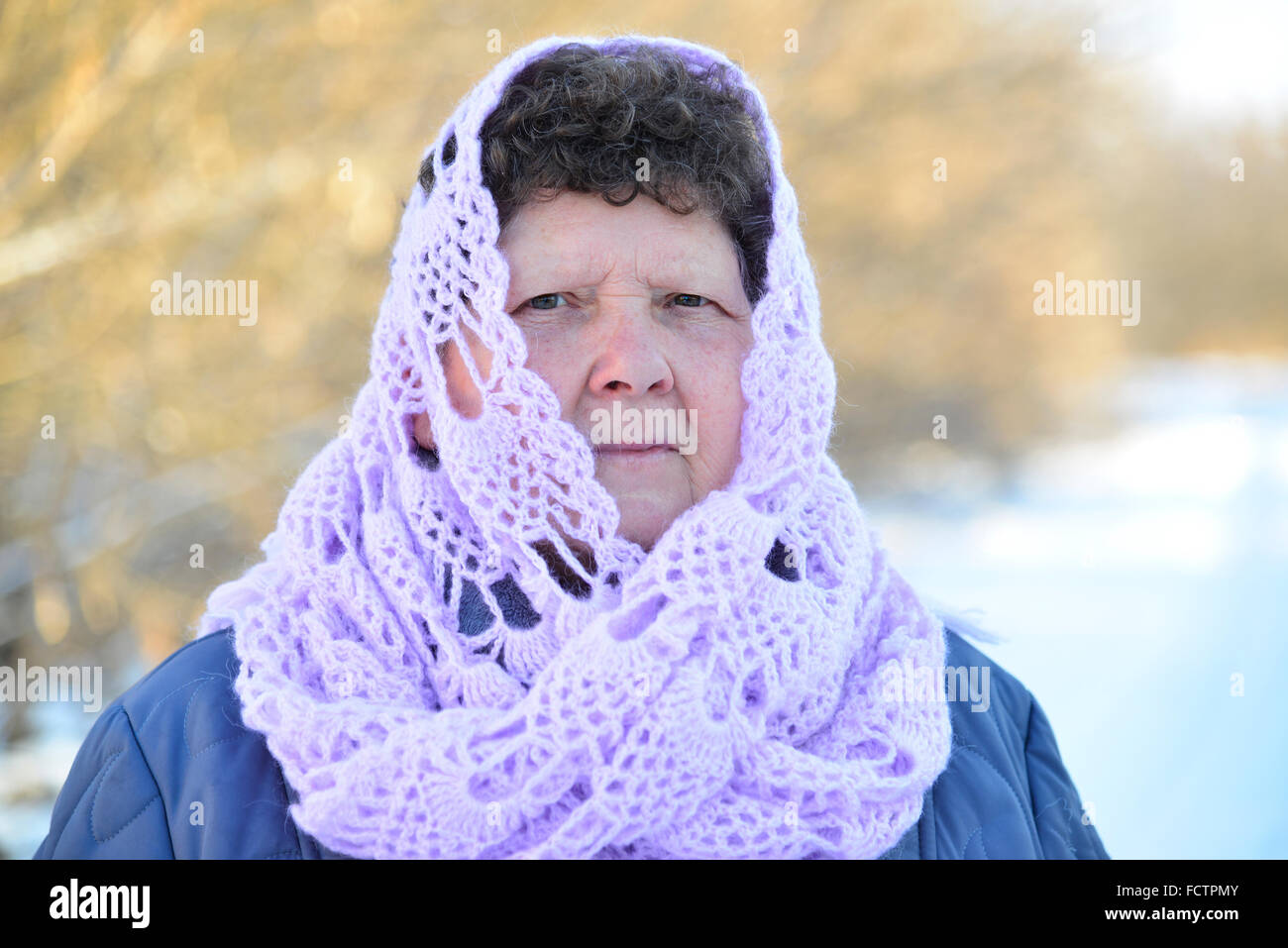 Elderly woman in lilac knitted scarf on her head outdoors Stock Photo