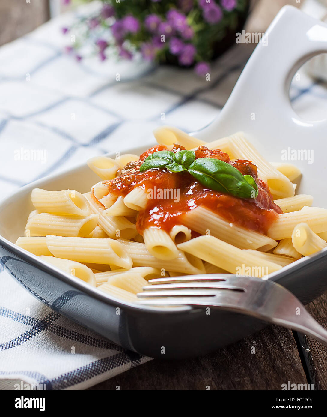 A plate of macaroni pasta tossed in a vibrant red tomato sauce and garnished with a sprig of basil.