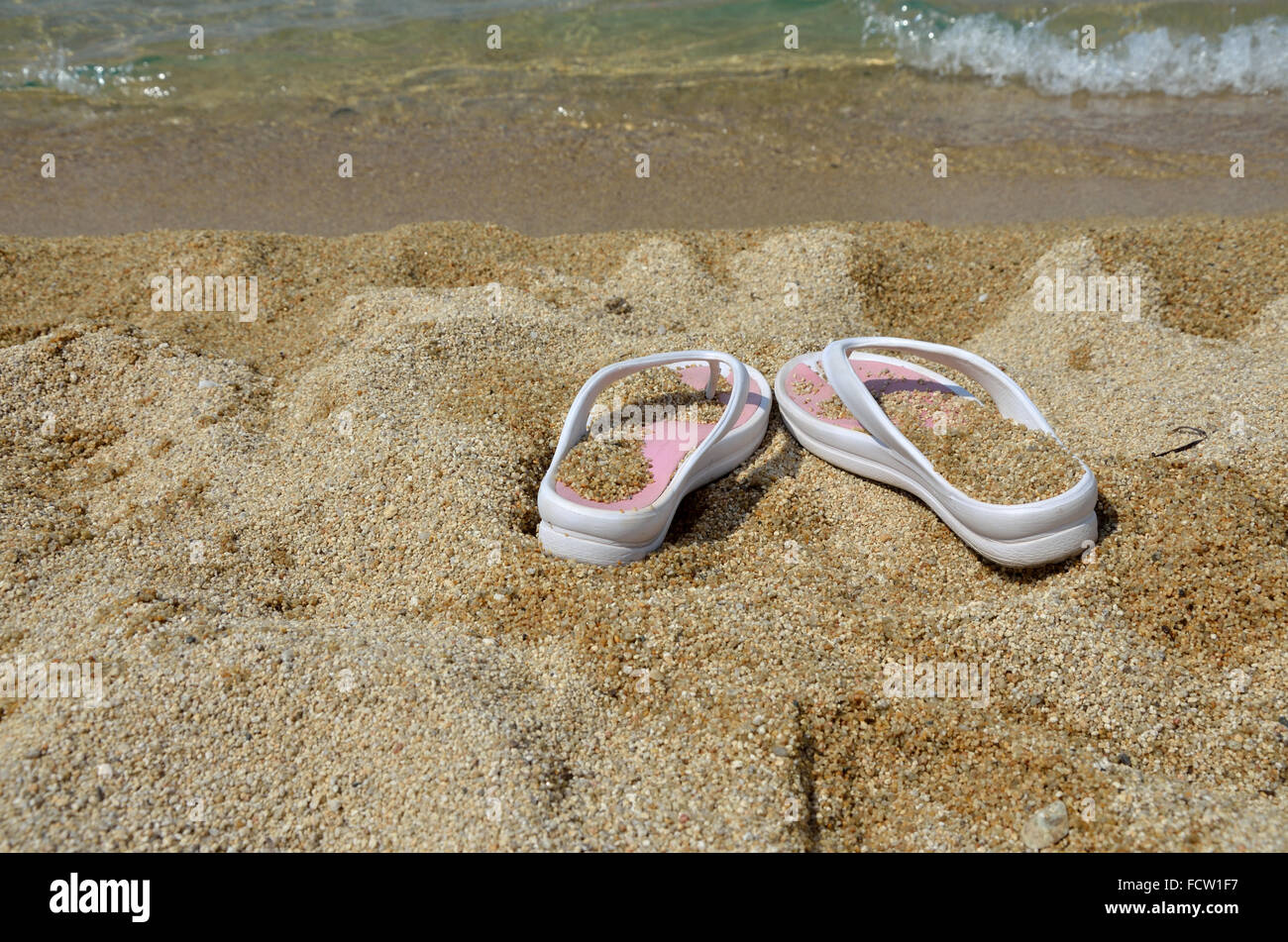 White-pink flip-flops on beach sand with sea shallow in background ...