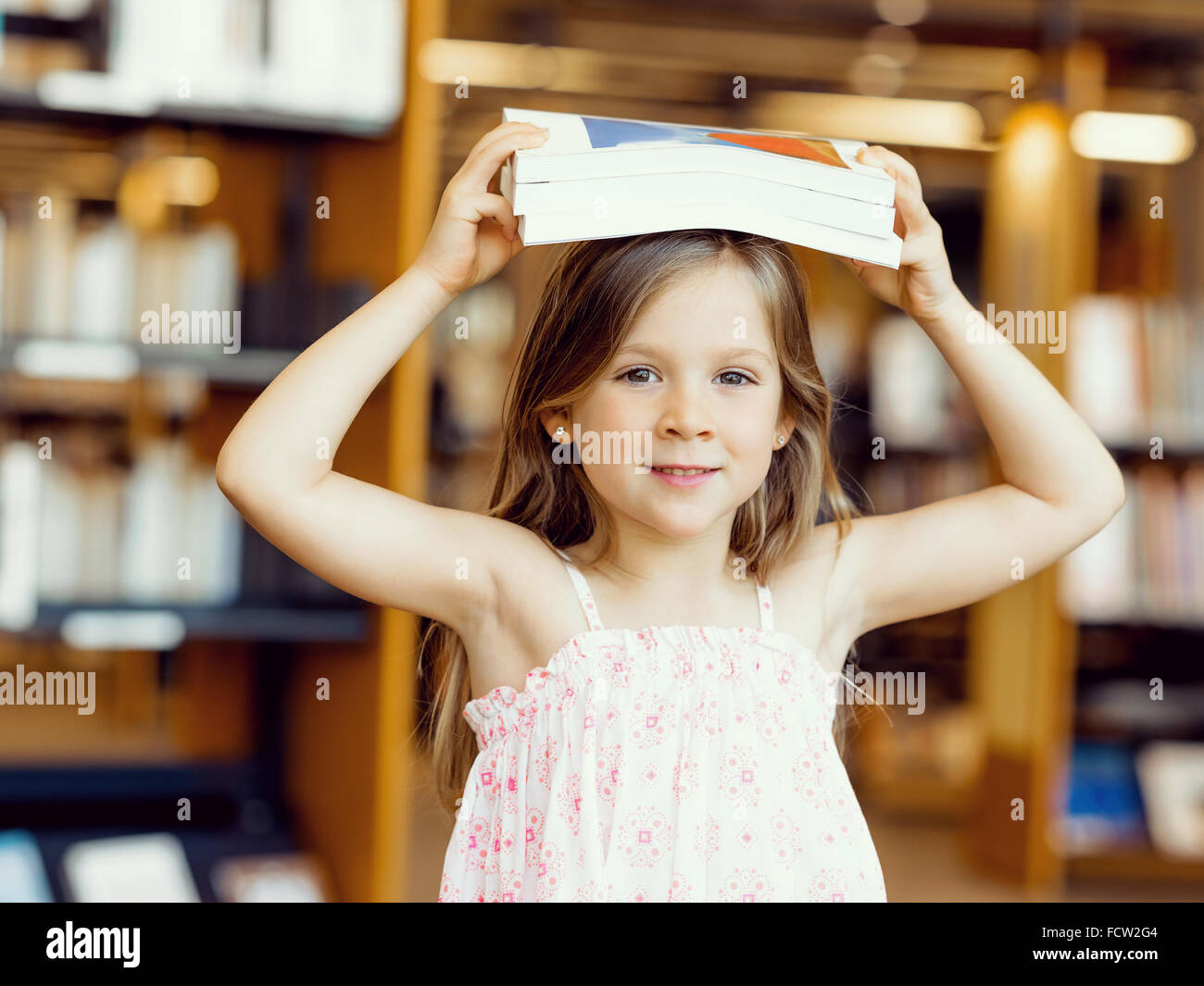 Little girl with a book on top of her head in library Stock Photo - Alamy