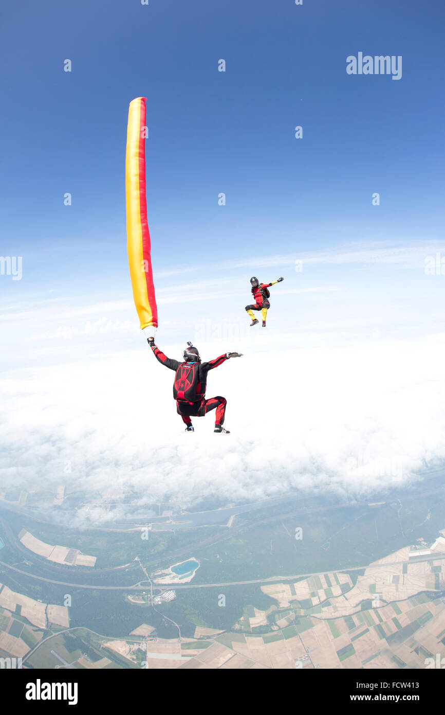 A crazy freefly skydiving team is playing with an air-tube in freefall together. Thereby they are falling with speed of 120 mph. Stock Photo