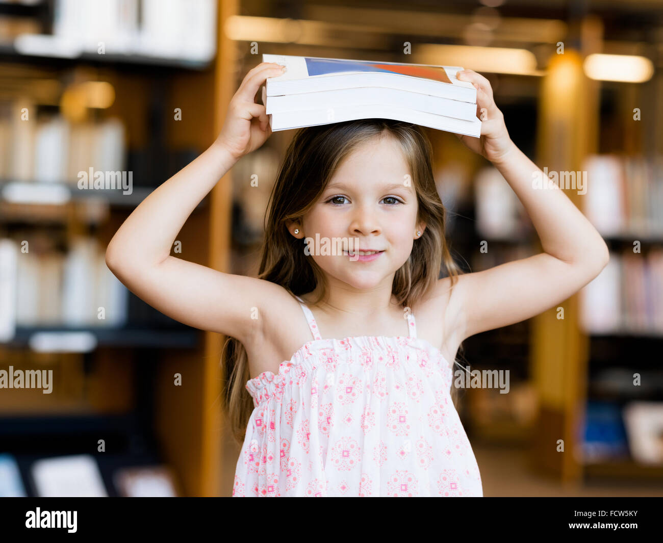 Little girl with a book on top of her head in library Stock Photo - Alamy