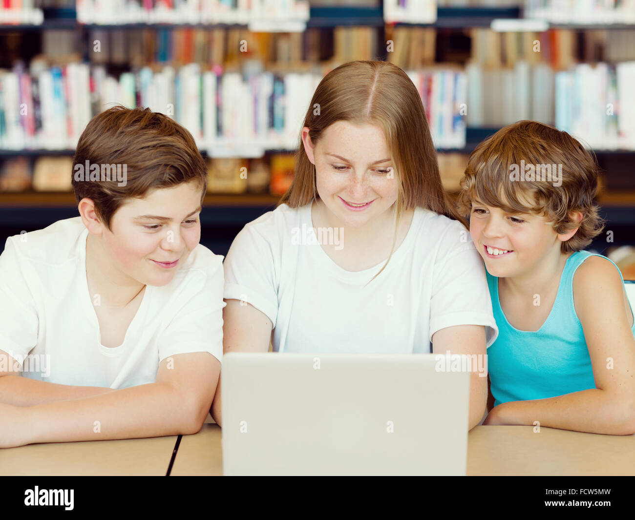 Three kids in library with notebook Stock Photo - Alamy