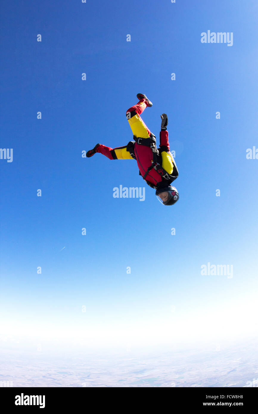 A skydiver girl is flying in a head-down position in the blue sky. Thereby she'll get a speed up to 150 mph downwards. Stock Photo