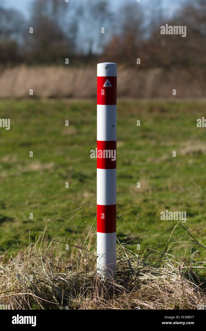 Striped red and white signal poles barricade in front of greenfield Stock Photo