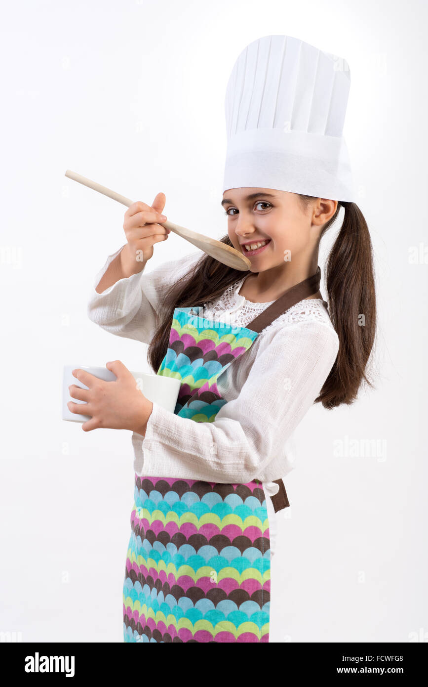 Laughing pretty little cook in a chefs toque and colorful apron standing Stock Photo