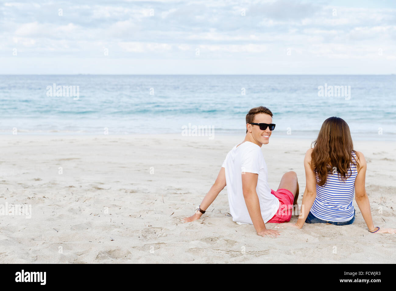 Romantic young couple sitting on the beach looking at the ocean Stock ...