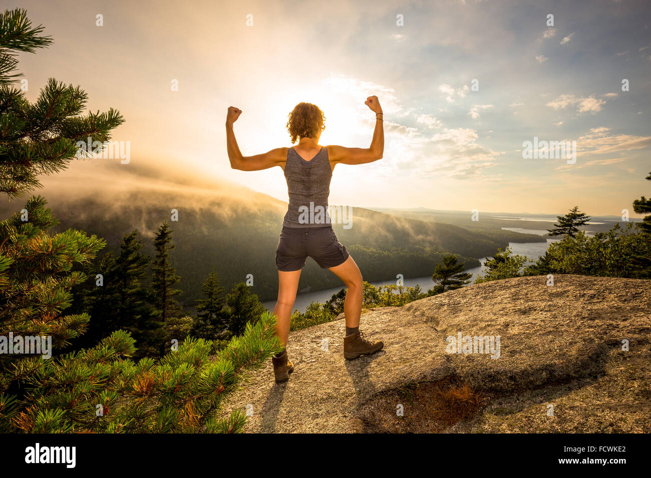 A young woman flexes on a mountaintop overlook in Acadia National Park, Mount Desert Island, Maine, New England, USA. Stock Photo