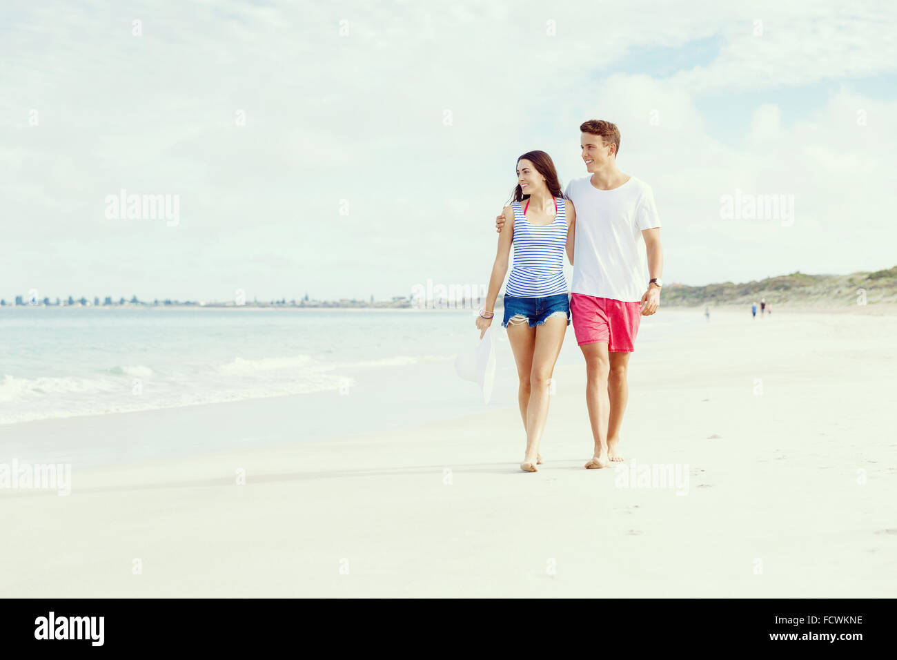 Romantic young couple on the beach walking along the shore Stock Photo ...