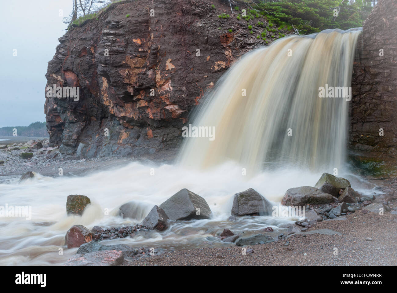 Springtime Nova Scotia coastline in June.   Waterfalls from cliff onto rocky pebble beach. Stock Photo